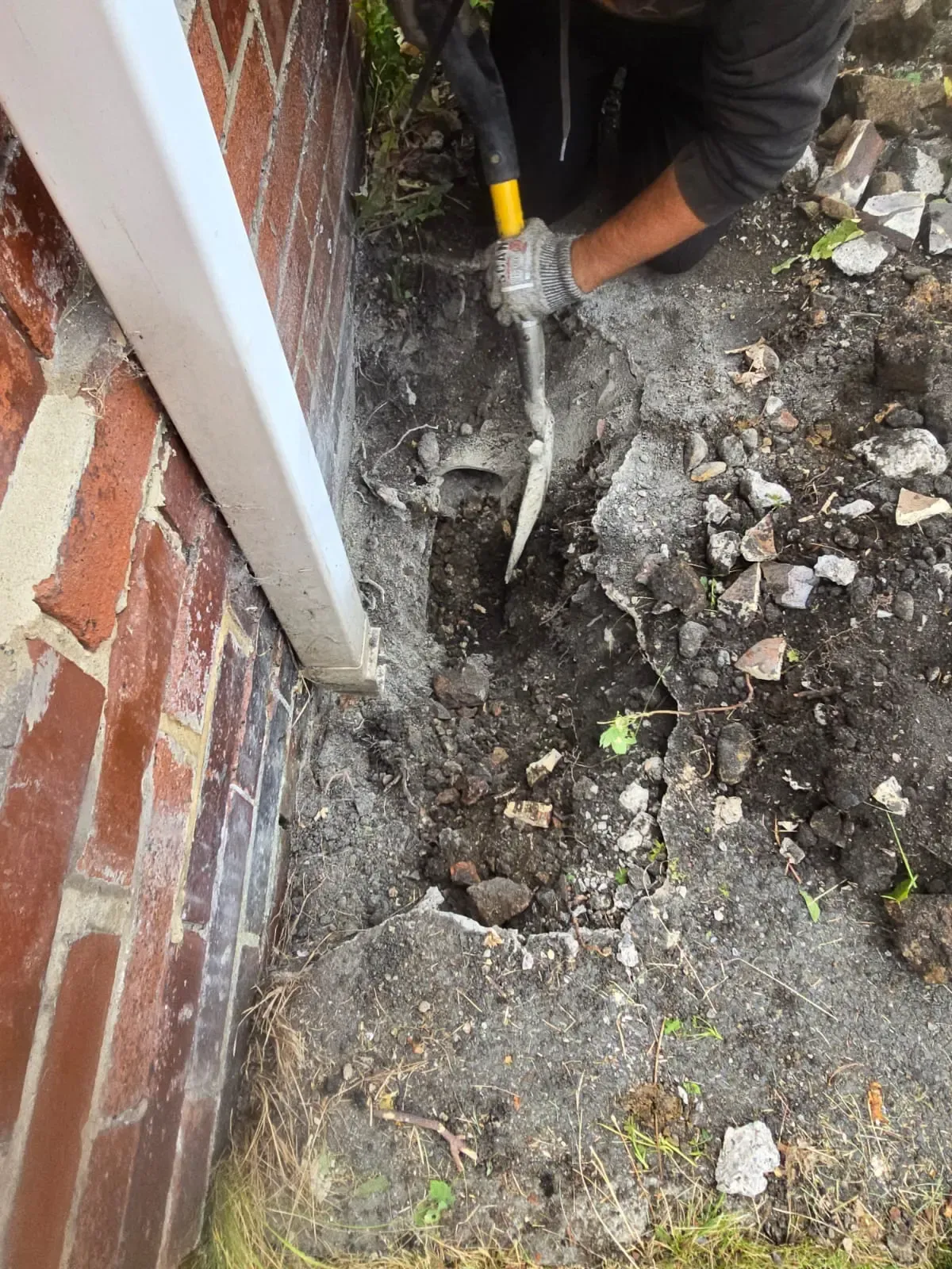APJ drainage engineer digging a trench next to an exterior wall to repair a collapsed drain.