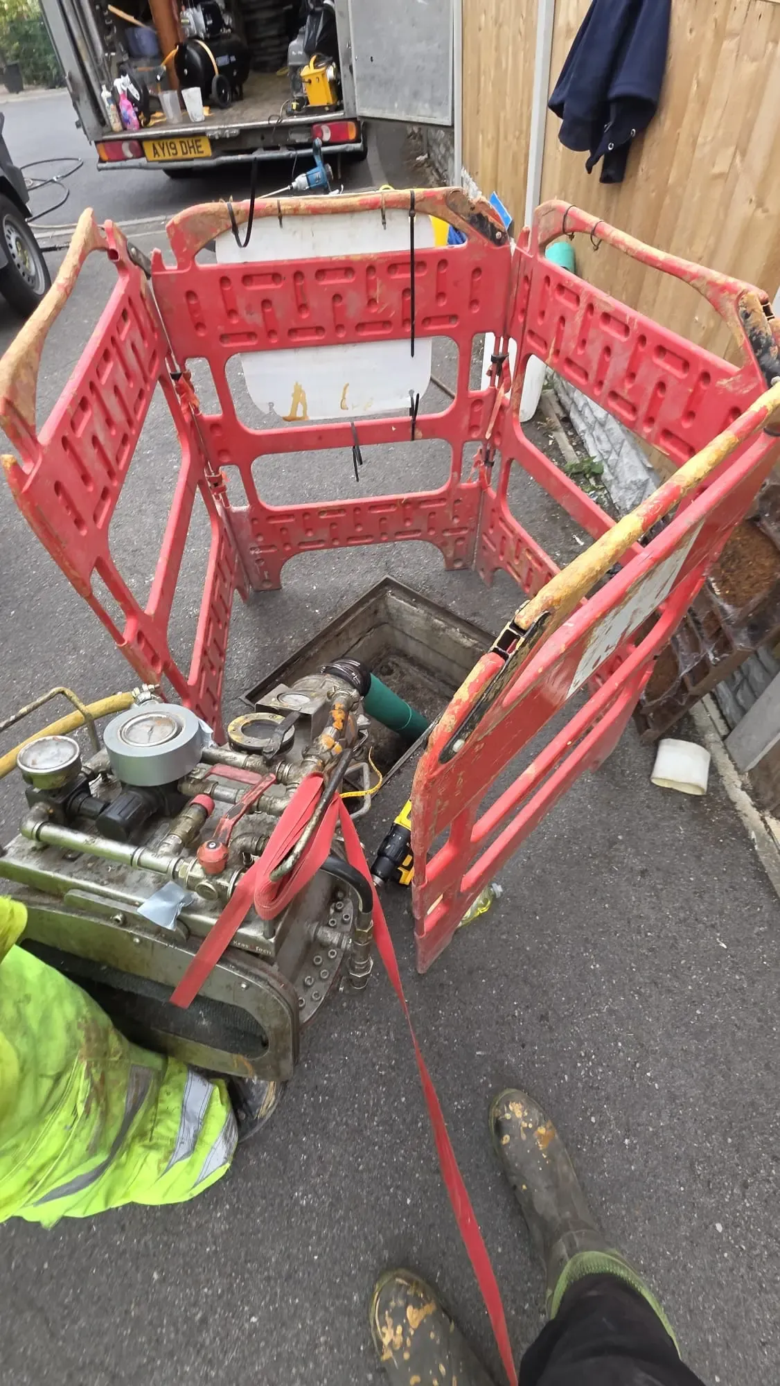 Specialist drainage equipment in use over an open manhole guarded by red safety barriers.