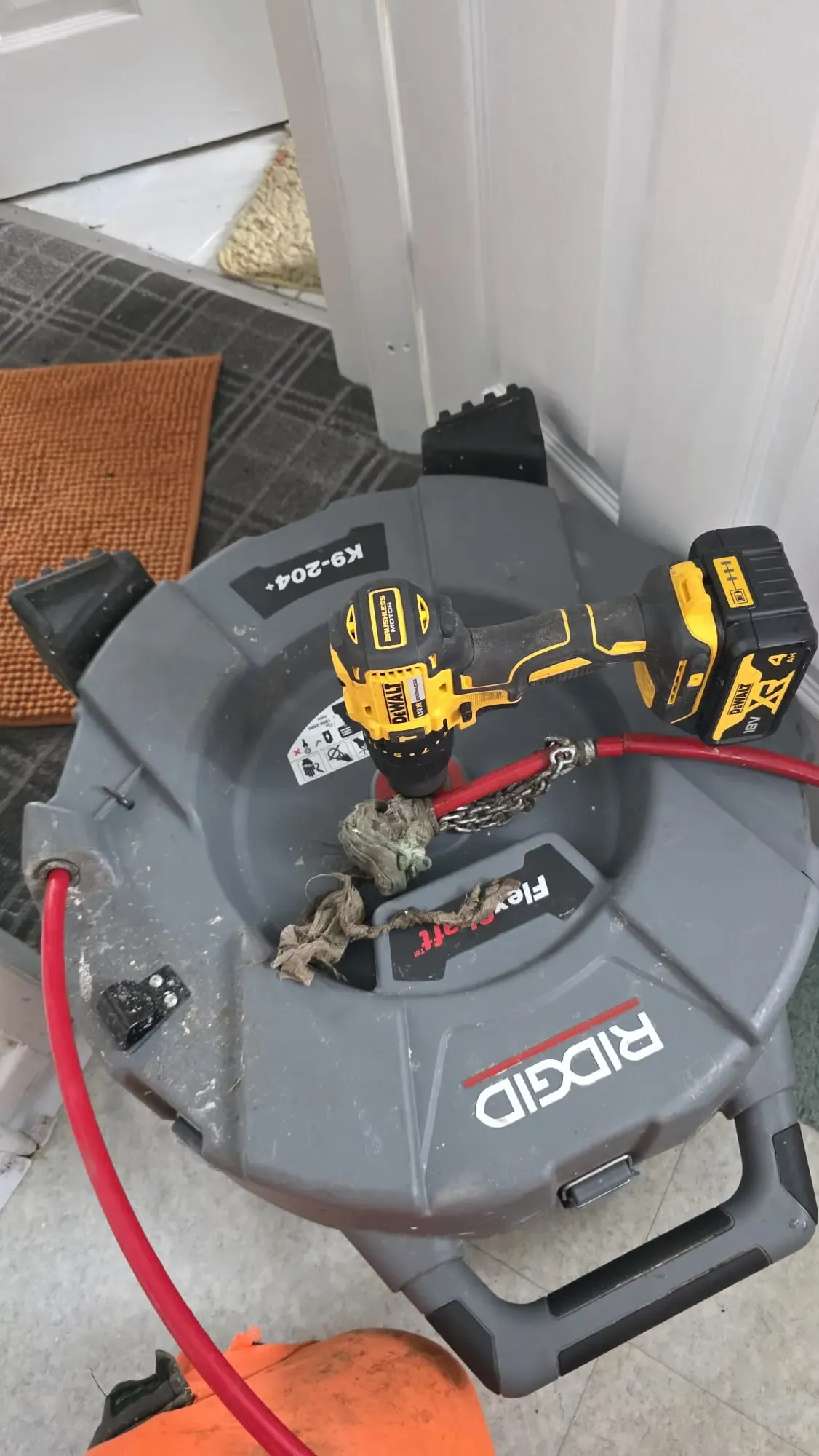 A Ridgid FlexShaft mechanical drain unblocking machine powered by a DeWalt cordless drill, showing debris removed from a pipe.